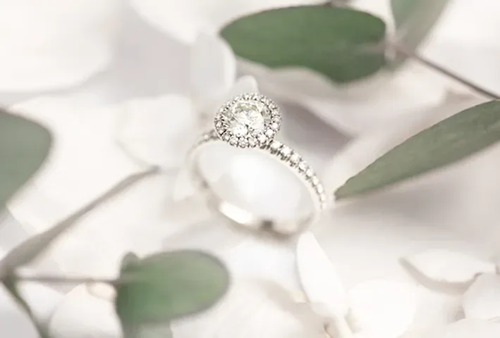Bague en diamants posée parmi des pétales blancs et des feuilles d'eucalyptus