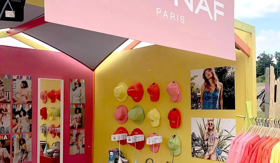 Stand Naf Naf rose et jaune, mur de bobs et de casquettes colorés