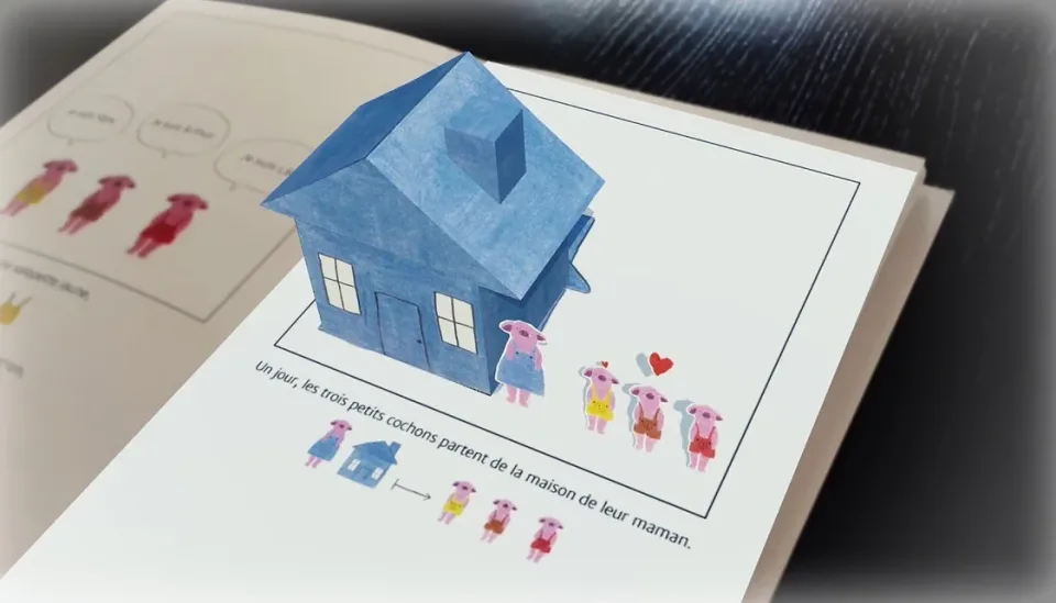 Page du livre en réalité augmentée : une maison bleue en volume surgit au-dessus de l'illustration