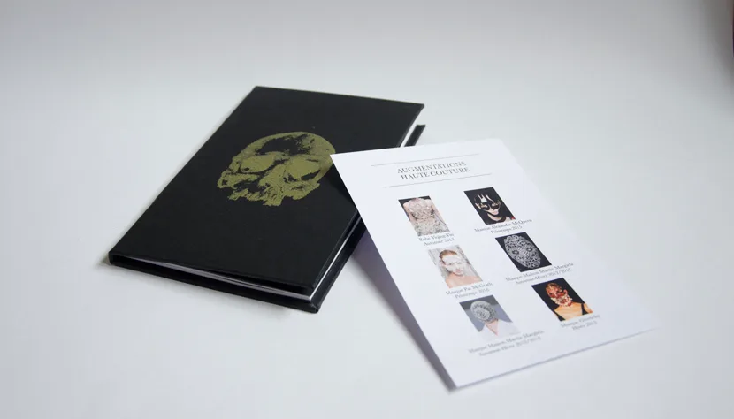 Livre noir au crâne doré et carte « Augmentations haute couture »
